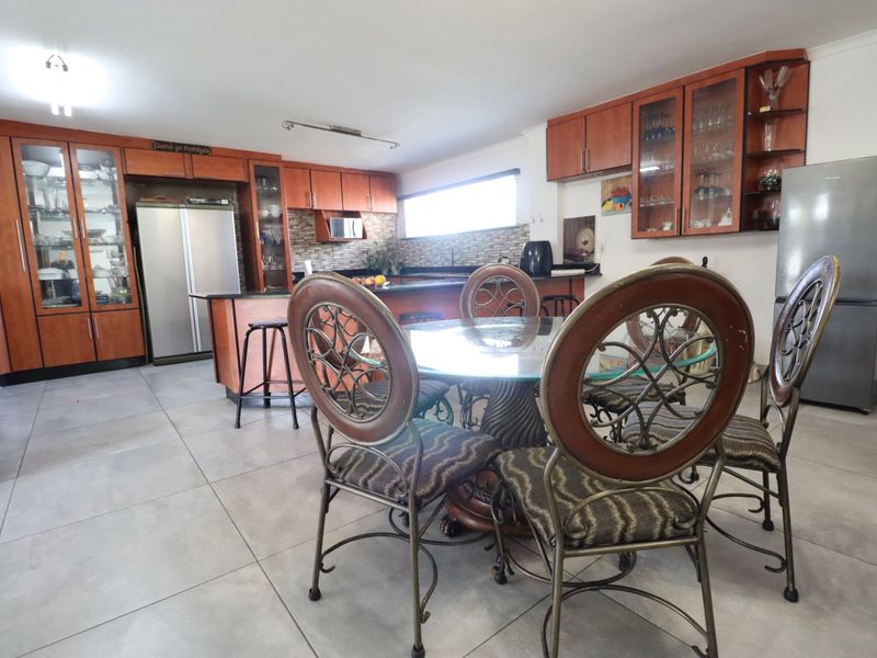 Spacious open-plan kitchen and dining area featuring extensive wooden cabinetry, stone countertops, and large format floor tiles.