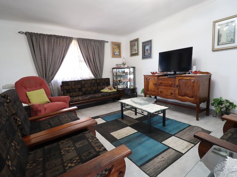 A well-maintained living room featuring neutral tiled flooring and large windows with curtain rails, providing a comfortable and functional space.