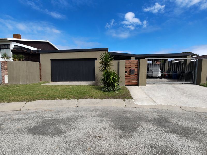 Front elevation of the property featuring a modern garage door, secure sliding gate, concrete driveway, and a well-maintained boundary wall.