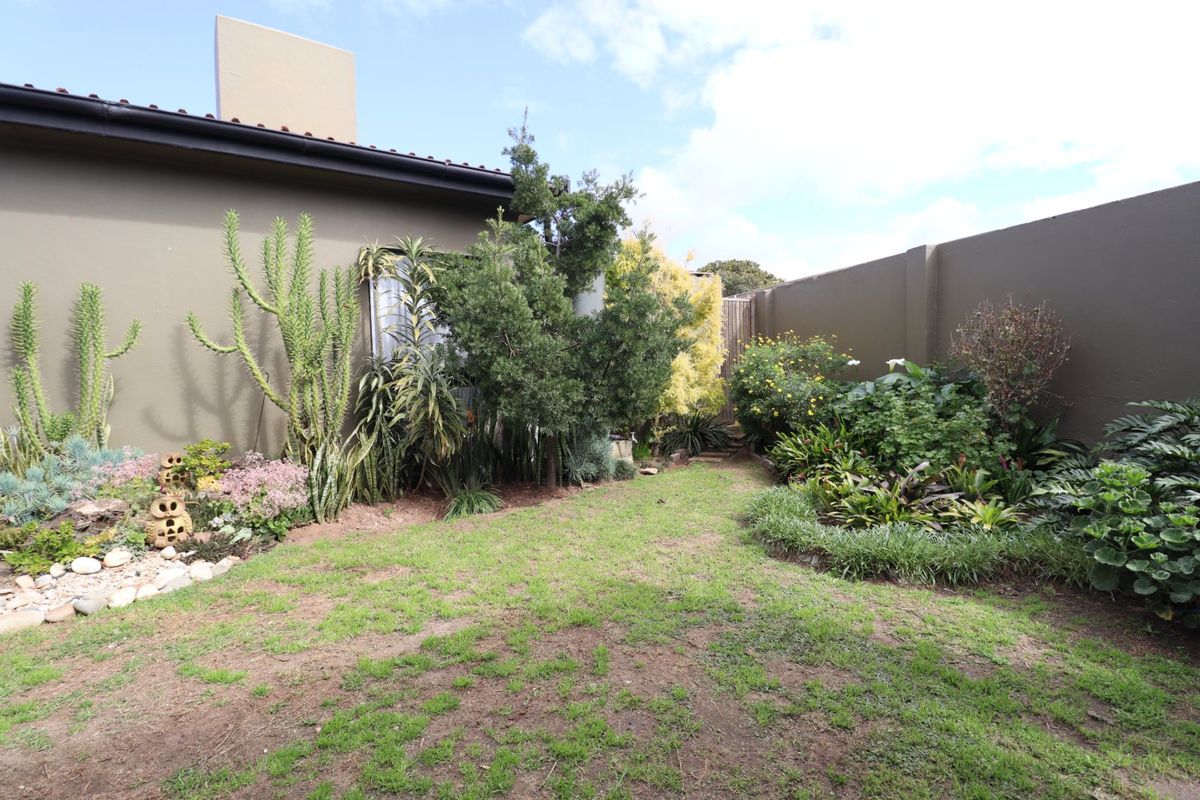 A private rear garden featuring established landscaping, a lawn area, and high boundary walls for privacy.
