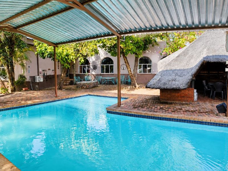 Outdoor pool area featuring a swimming pool, brick paving, and a traditional thatched lapa structure for entertainment.