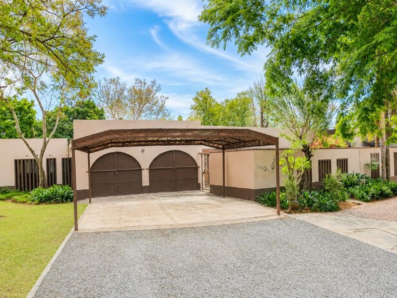 Front exterior view of the property featuring a double garage, covered carport, paved and gravel driveway, and a well-maintained garden.