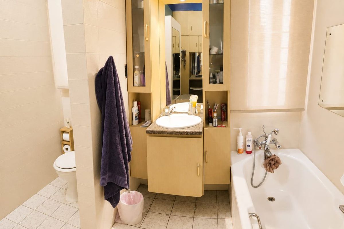 A functional bathroom featuring a built-in vanity with integrated mirror, a standard bathtub with shower mixer, and a separate toilet area with tiled finishes.