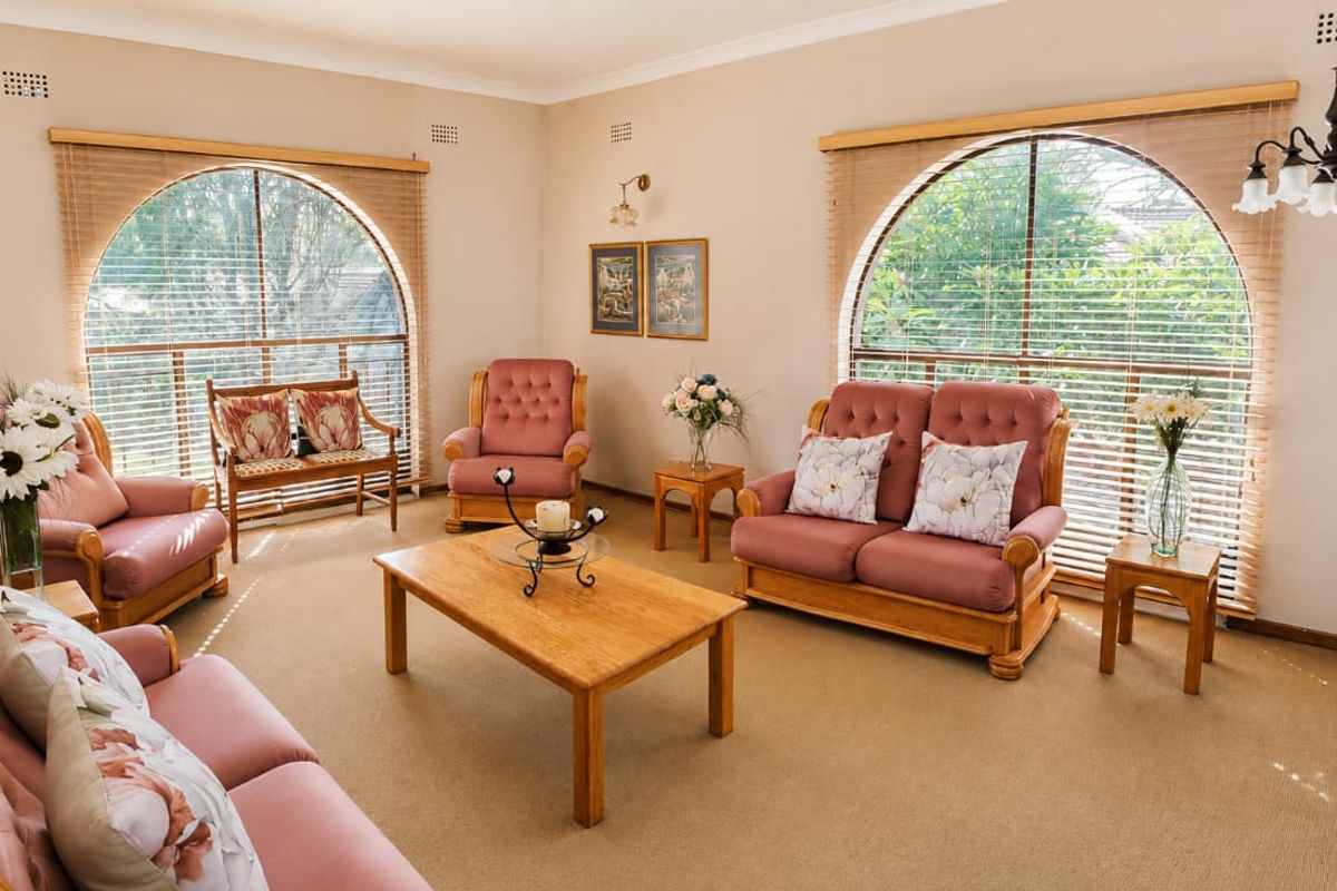 A spacious living room featuring distinctive arched windows, neutral wall tones, and carpeted flooring, offering a bright and comfortable atmosphere.