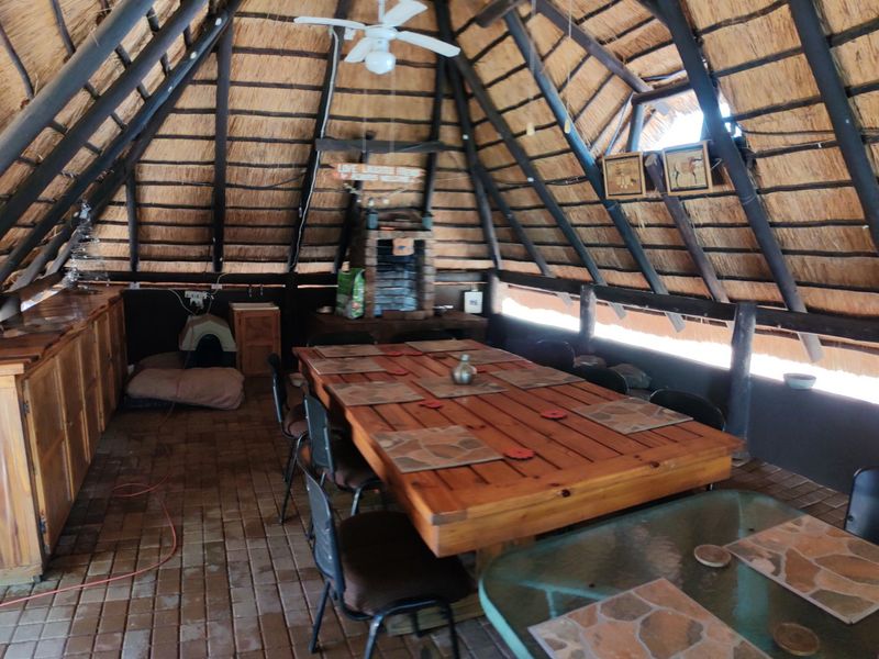 Spacious outdoor entertainment area featuring a traditional thatched roof, exposed timber rafters, brick flooring, and a built-in brick fireplace.