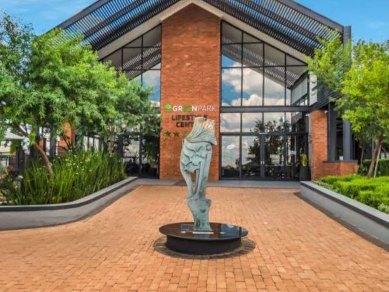 The front entrance of the Greenpark Lifestyle Centre, featuring a modern brick and glass facade with a paved walkway and landscaped surroundings.