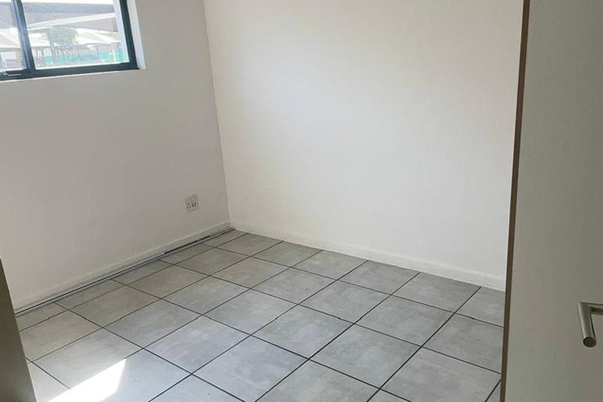 A clean, empty bedroom featuring neutral grey floor tiles, a modern pendant light, and a window providing natural light.