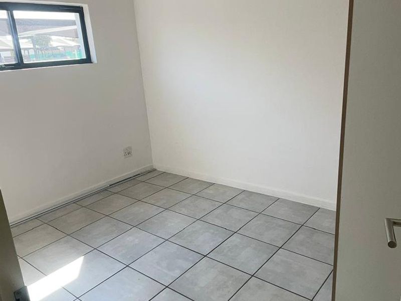 A clean, empty bedroom featuring neutral grey floor tiles, a modern pendant light, and a window providing natural light.