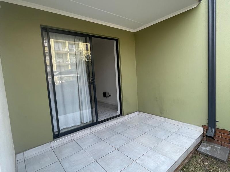 A clean, tiled ground-floor patio area featuring a sliding glass door entrance and a functional downpipe, offering a simple outdoor space.