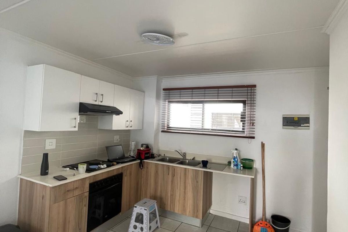 A functional kitchen featuring modern wood-look cabinetry, white upper cabinets, tiled flooring, and integrated appliances including an oven and extractor fan.
