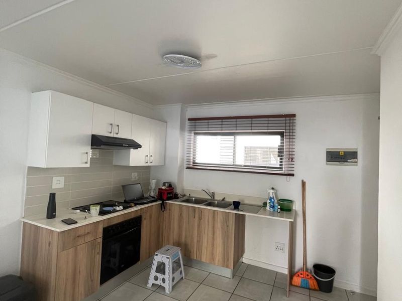 A functional kitchen featuring modern wood-look cabinetry, white upper cabinets, tiled flooring, and integrated appliances including an oven and extractor fan.