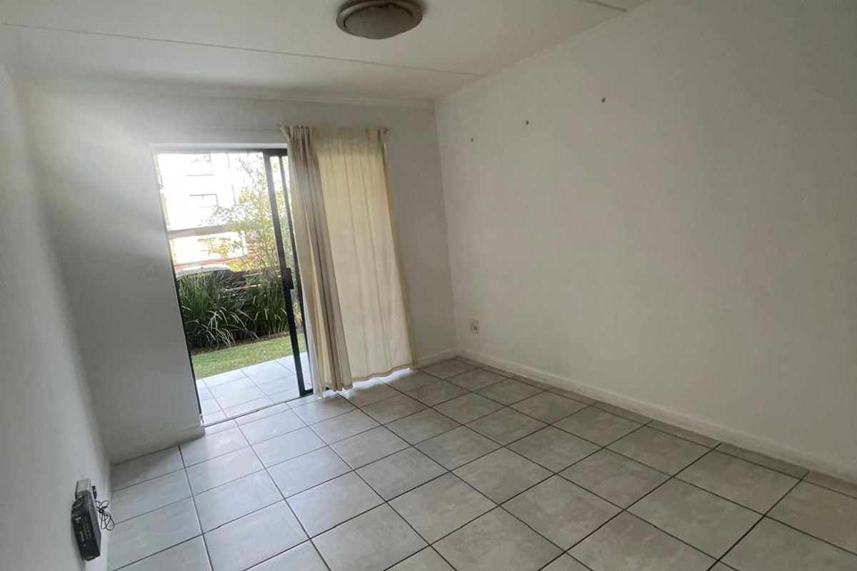 An empty living room featuring neutral tiled flooring and a sliding glass door providing direct access to an outdoor patio area.
