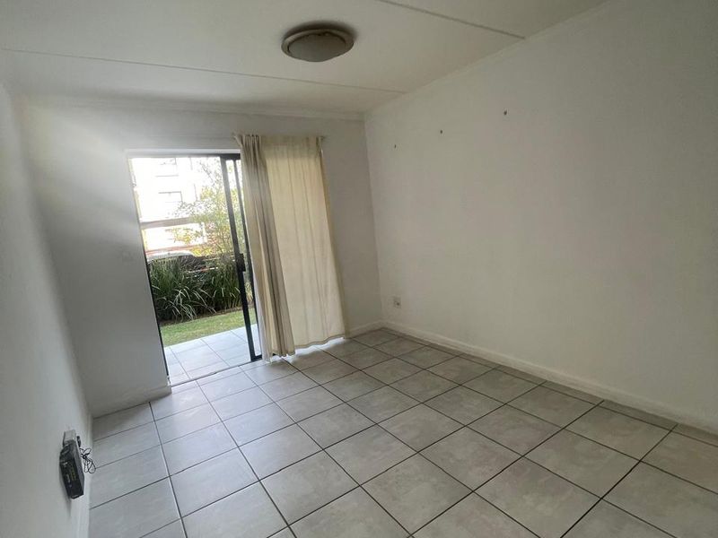 An empty living room featuring neutral tiled flooring and a sliding glass door providing direct access to an outdoor patio area.