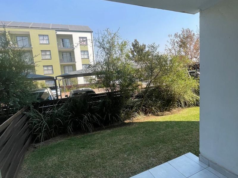 A covered patio area featuring tiled flooring, overlooking a private garden space with a wooden fence boundary.