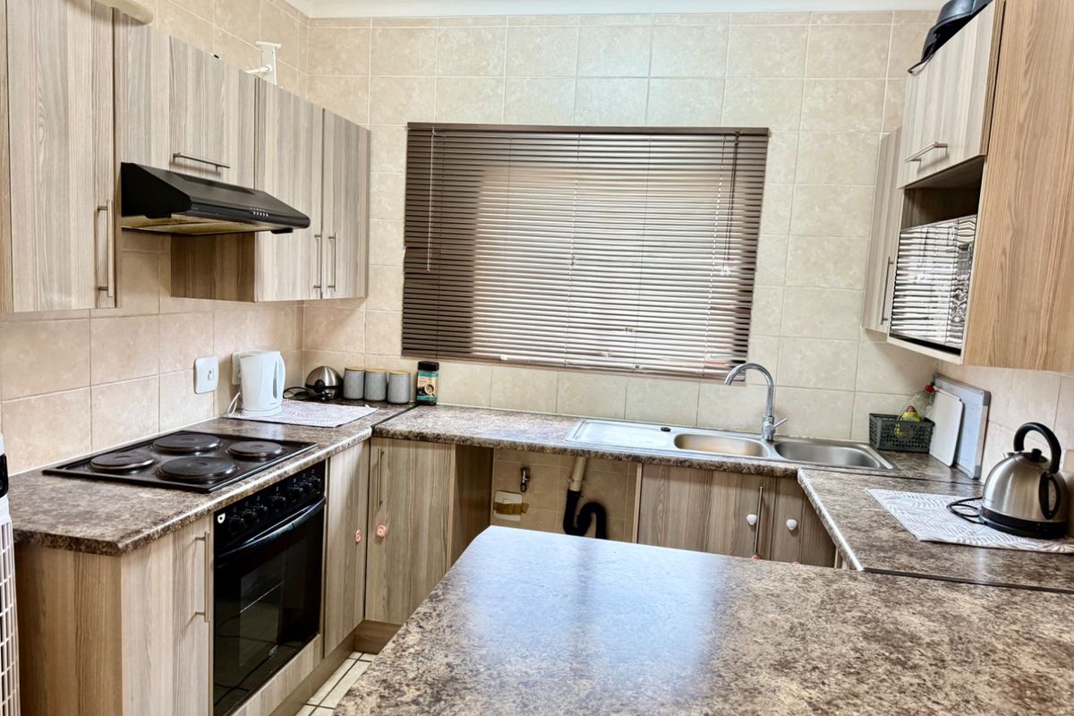 Functional kitchen featuring laminate cabinetry, stone-look countertops, built-in oven with hob, and a double bowl sink with tiled backsplash.