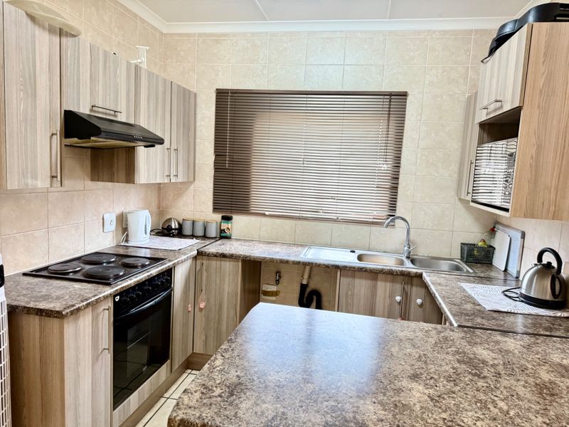 Functional kitchen featuring laminate cabinetry, stone-look countertops, built-in oven with hob, and a double bowl sink with tiled backsplash.