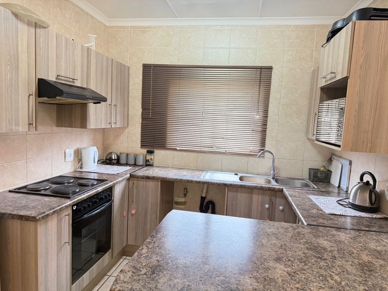 Functional kitchen featuring laminate cabinetry, stone-look countertops, built-in oven with hob, and a double sink with tiled backsplash.