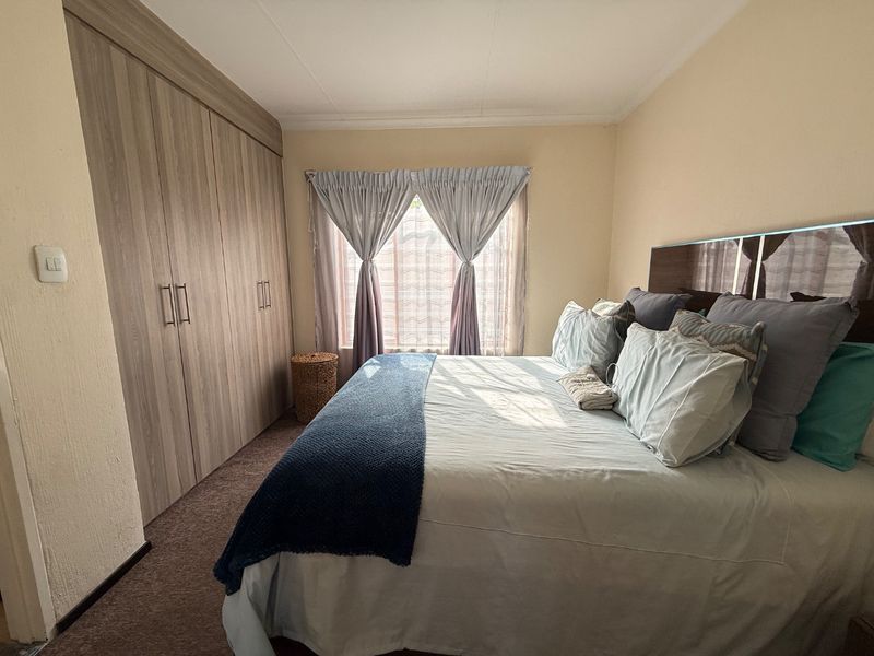 A functional bedroom featuring built-in wooden cupboards and carpeted flooring, providing ample storage space and a comfortable layout.