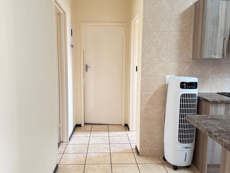 A functional hallway area featuring tiled flooring and access to adjacent rooms, with a partial view of kitchen cabinetry and granite countertops.