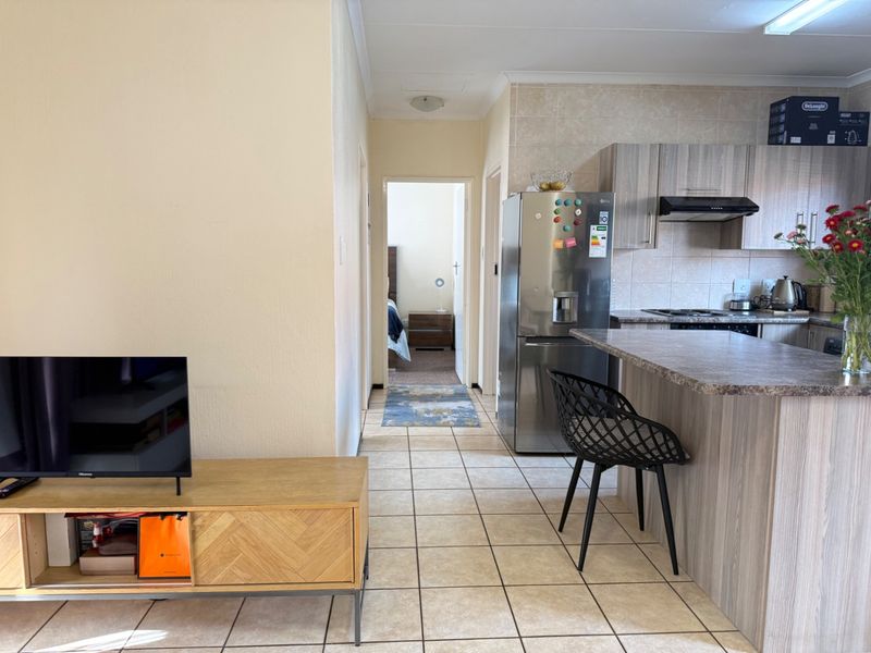 Open plan living area featuring a kitchen with wood-look cabinetry, breakfast bar, and tiled flooring, leading to a hallway and bedroom.