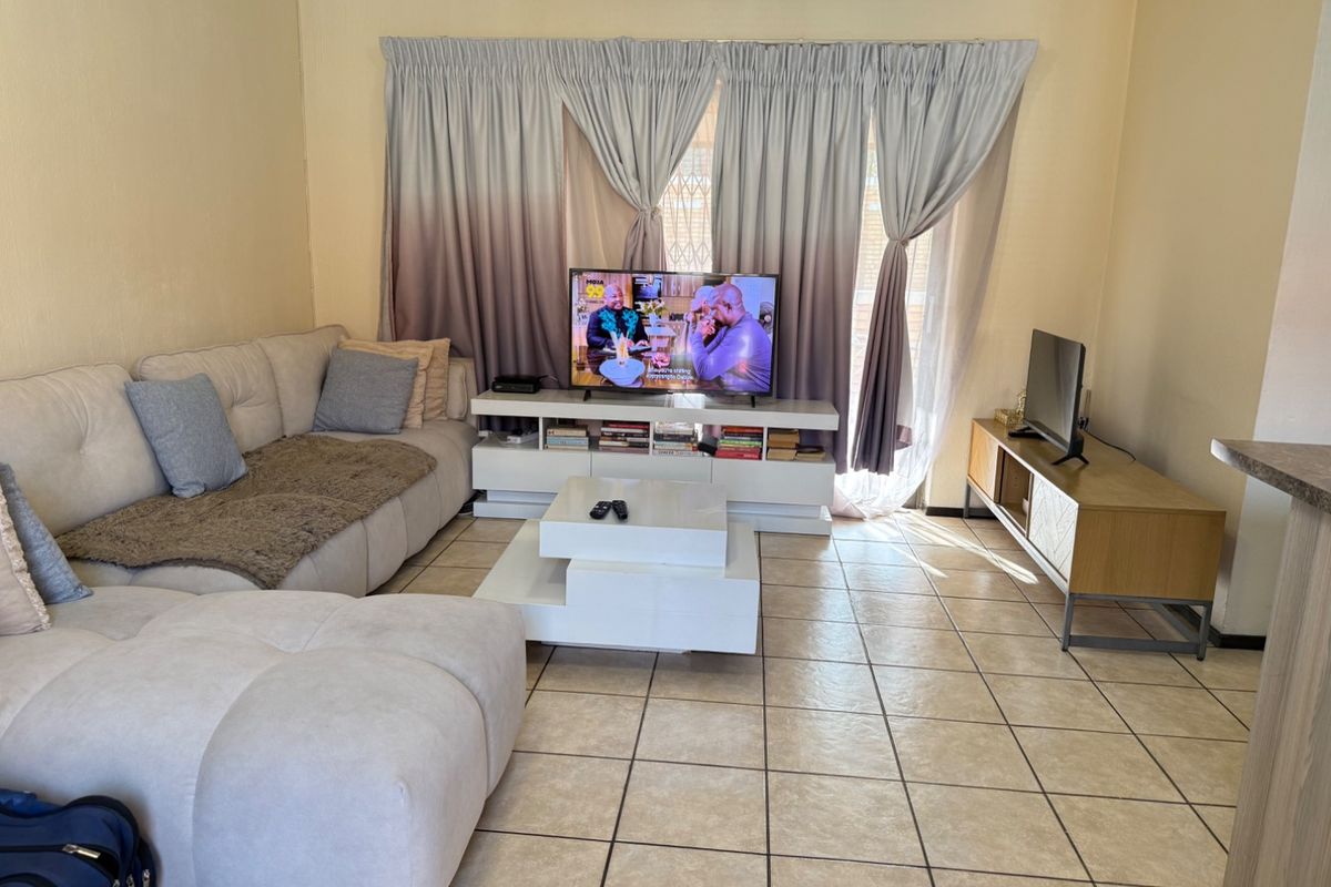 A comfortable living room featuring tiled flooring and large windows with curtain treatments, providing a functional and well-lit space for relaxation.