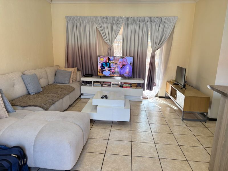 A comfortable living room featuring tiled flooring and large windows with curtain treatments, providing a functional and well-lit space for relaxation.