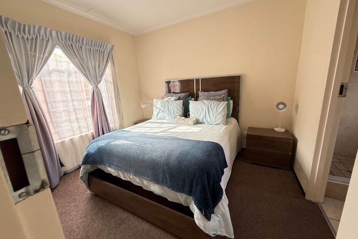 A standard bedroom featuring carpeted flooring, coved ceilings, and a window with curtain rails. The room includes an adjacent en-suite bathroom area.