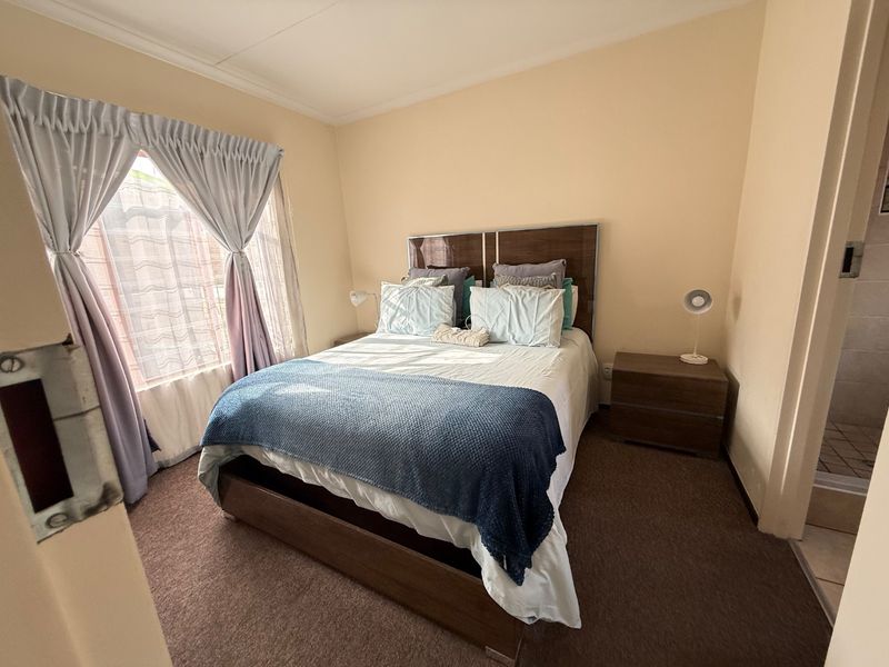 A standard bedroom featuring carpeted flooring, coved ceilings, and a window with curtain rails. The room includes an adjacent en-suite bathroom area.
