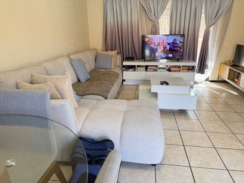 A comfortable living room featuring ceramic floor tiles and a sliding glass door with security gate, providing access to the exterior.
