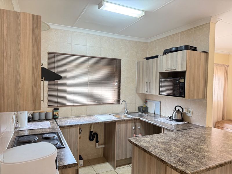 Functional kitchen featuring laminate cabinetry, tiled backsplash, built-in electric hob, and a stainless steel sink with an open under-counter plumbing area.