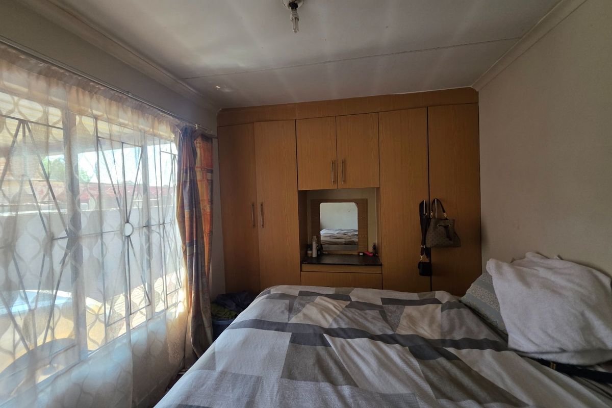 A bedroom featuring built-in wooden cupboards with a central vanity area and a window fitted with a security gate.