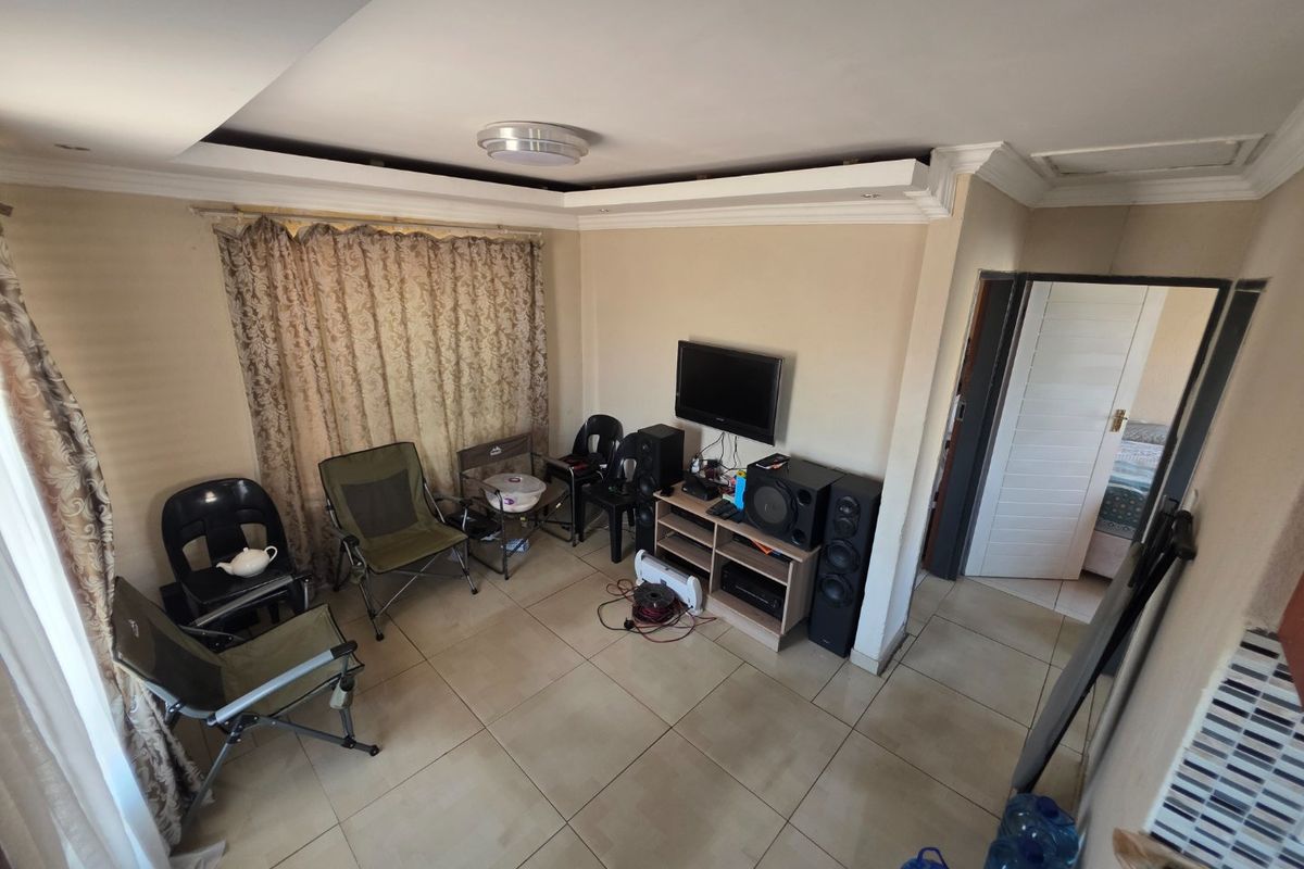A living room featuring tiled flooring, recessed ceiling details with cove molding, and access to an adjacent room.