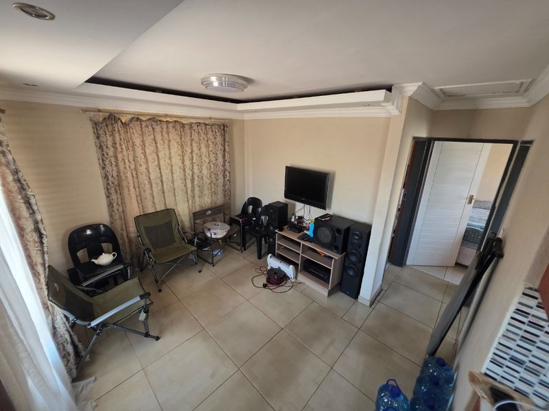 A living room featuring tiled flooring, recessed ceiling details with cove molding, and access to an adjacent room.