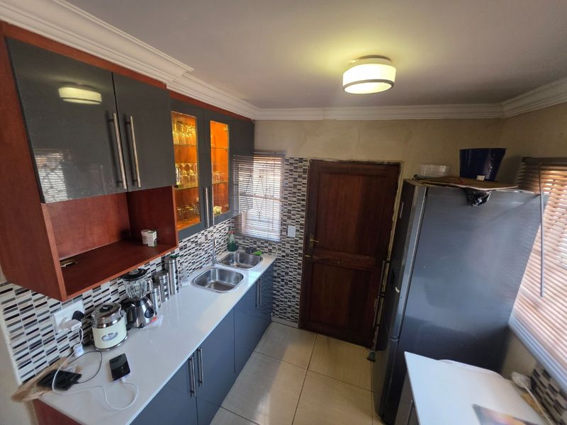 A functional kitchen featuring modern grey cabinetry, a double stainless steel sink, mosaic tile backsplash, and ceramic flooring with direct access to an exterior door.