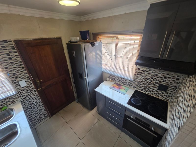 Compact kitchen featuring modern grey cabinetry, mosaic tile backsplash, built-in electric oven and hob, and tiled flooring.