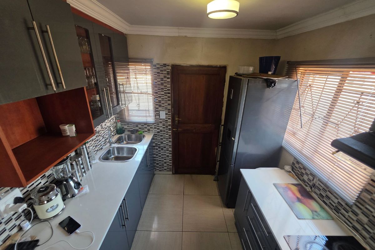 A functional kitchen featuring modern grey cabinetry, white countertops, double stainless steel sinks, and tiled backsplash with convenient access to an exterior door.