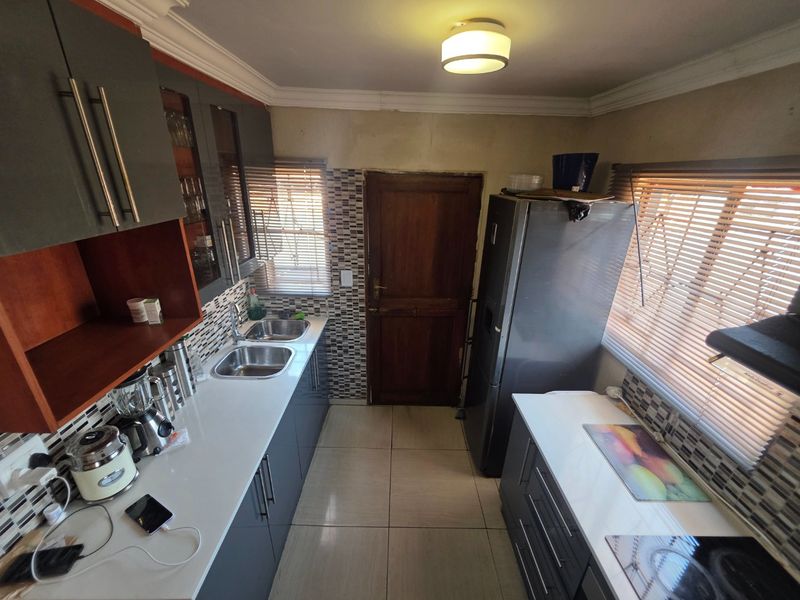 A functional kitchen featuring modern grey cabinetry, white countertops, double stainless steel sinks, and tiled backsplash with convenient access to an exterior door.