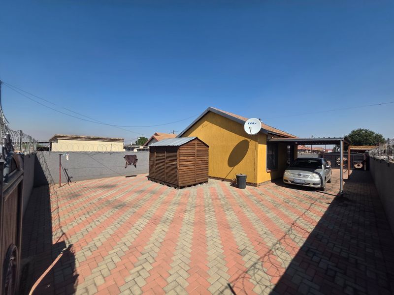 Rear exterior view of the property featuring a paved courtyard, carport, and secure perimeter walling with razor wire.