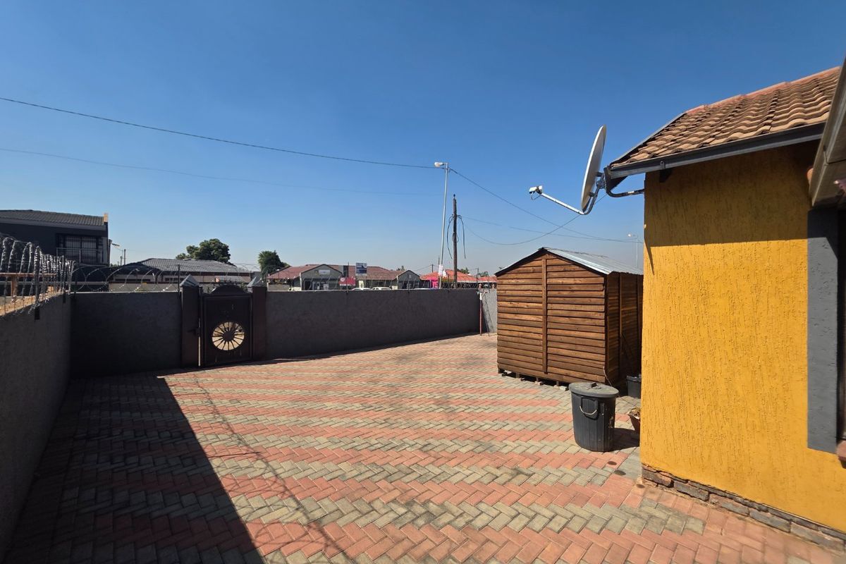 A paved rear courtyard area featuring a perimeter wall with security razor wire, a satellite dish, and a tiled roof structure.