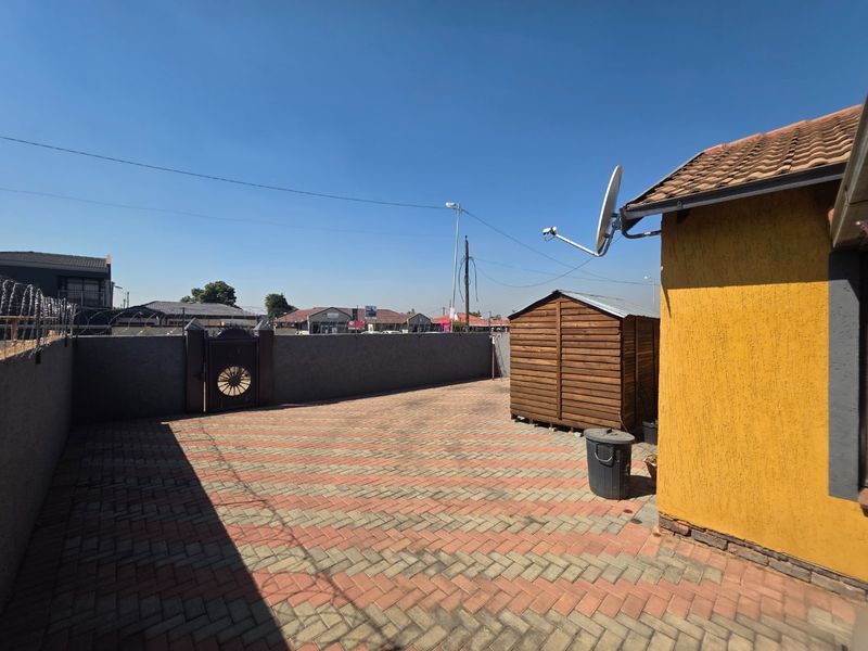 A paved rear courtyard area featuring a perimeter wall with security razor wire, a satellite dish, and a tiled roof structure.