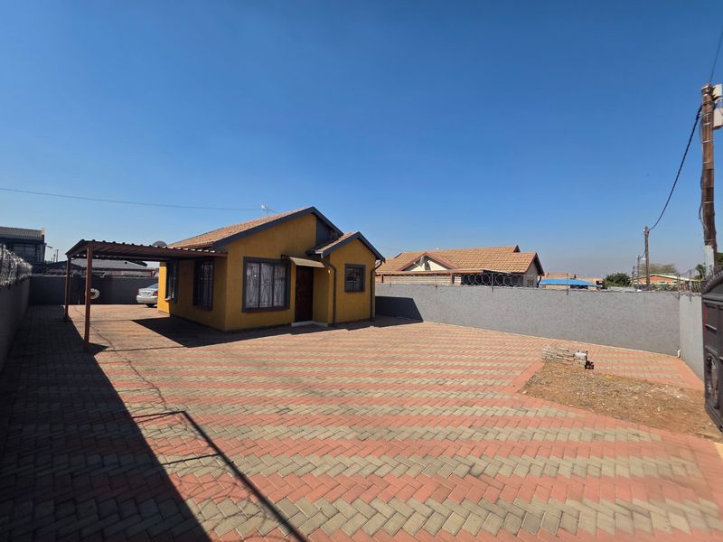 Front view of a detached house featuring a paved driveway, attached carport, and secure perimeter walling with razor wire.