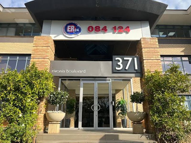 Front entrance of a commercial building featuring glass double doors, brick pillars, and prominent signage.