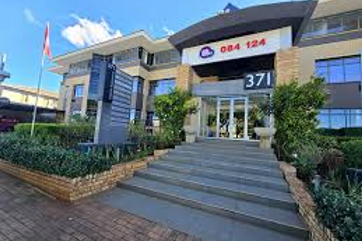 Front facade of a commercial office building featuring a paved entrance, stone retaining walls, and prominent street-facing signage.