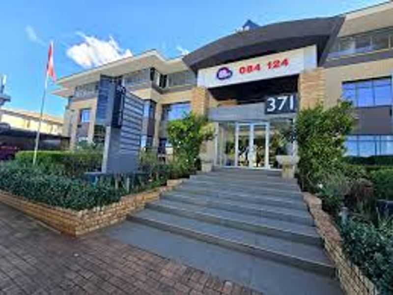 Front facade of a commercial office building featuring a paved entrance, stone retaining walls, and prominent street-facing signage.