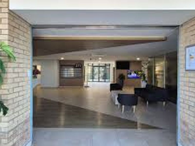 A welcoming commercial building entrance featuring a brick facade, modern tiled flooring, and a spacious lobby area with recessed lighting.