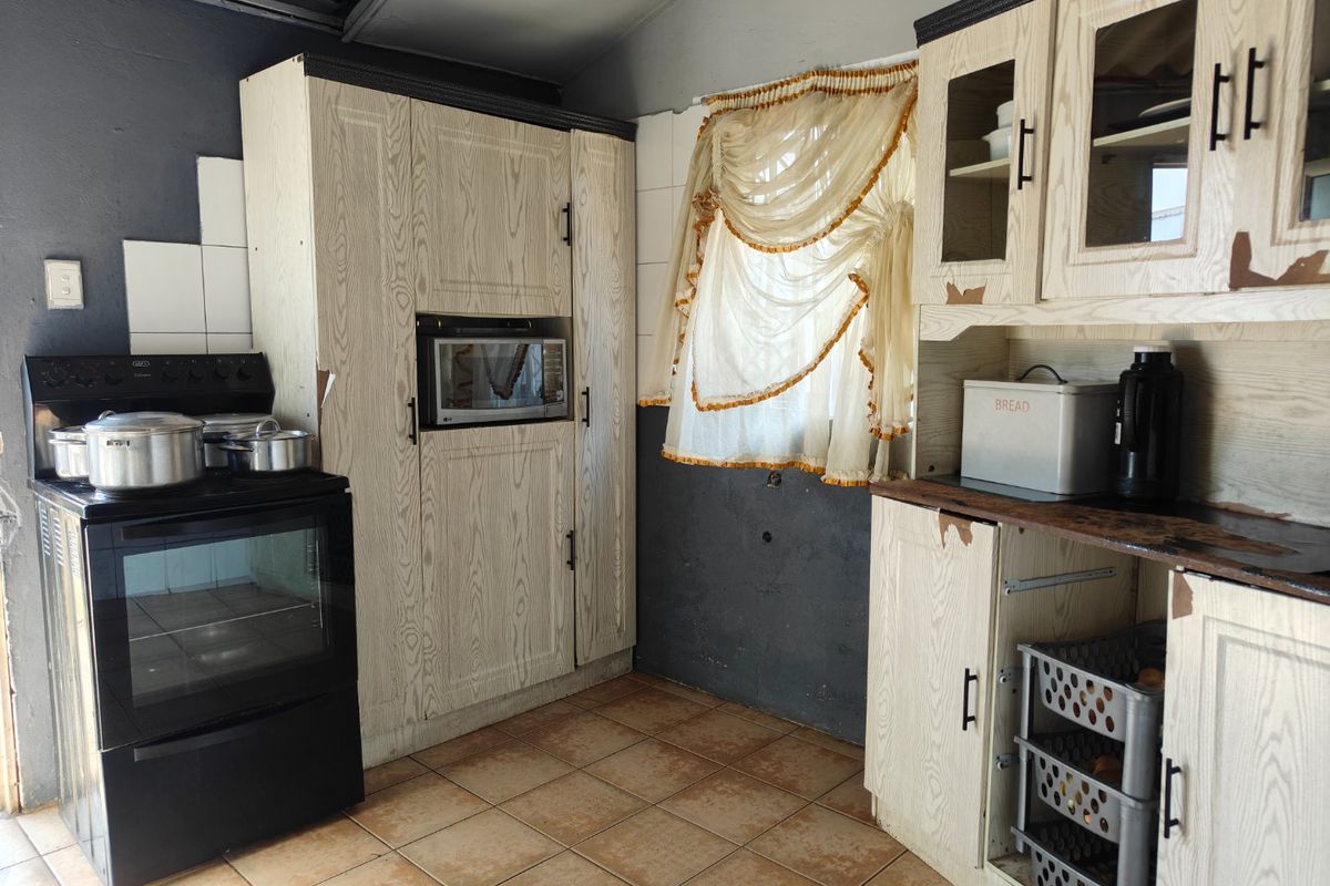 A dated kitchen featuring wood-grain cabinetry, tiled flooring, and a freestanding oven, showing signs of wear and requiring cosmetic updates.
