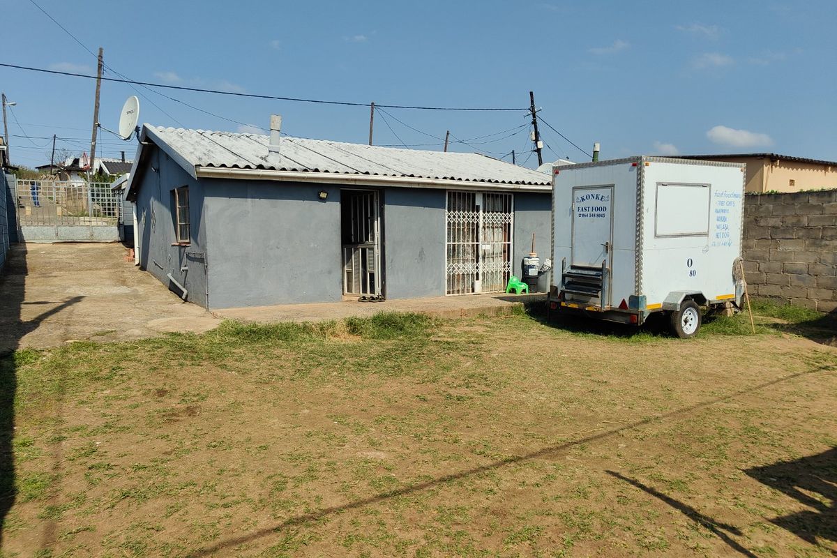 Rear view of a single-story house featuring a corrugated metal roof, security gates, and a concrete patio area set within a fenced yard.