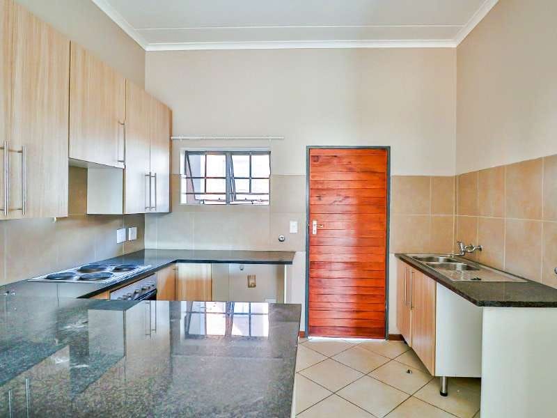 A functional kitchen featuring laminate cabinetry, granite countertops, an electric hob, built-in oven, and a double bowl sink with tiled splashbacks.