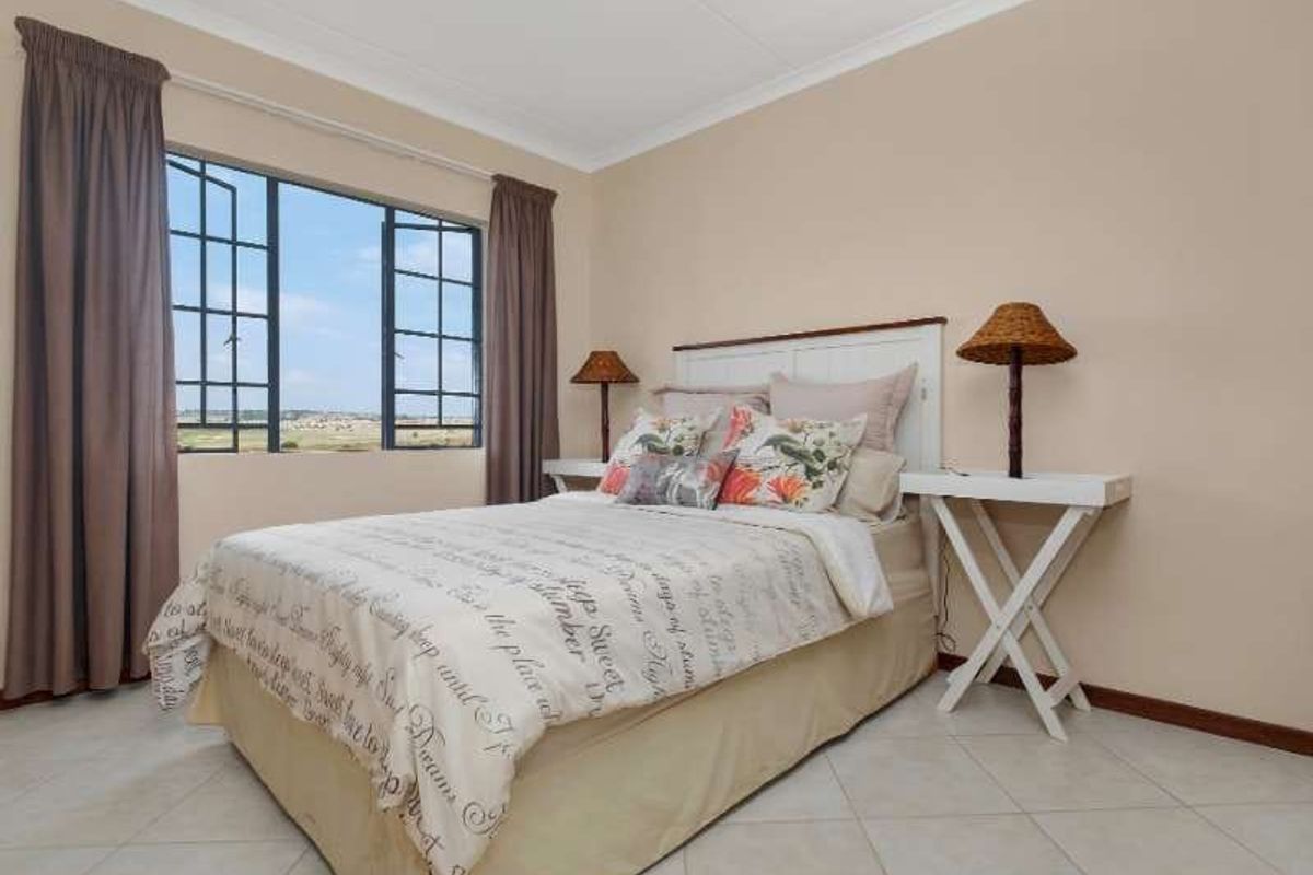 A well-maintained bedroom featuring tiled flooring, coved ceilings, and large casement windows that provide natural light and exterior views.