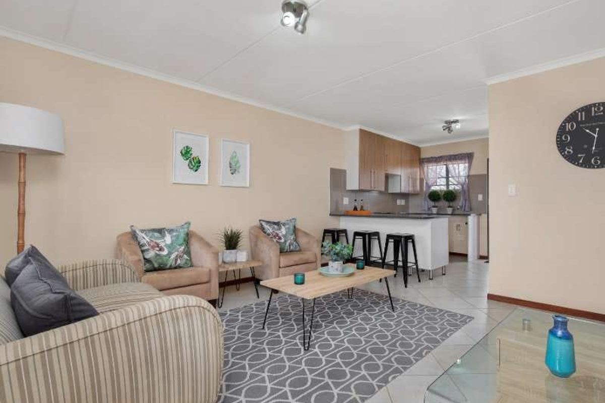 An open-plan living area featuring a modern kitchen with a breakfast island, tiled flooring, and neutral wall finishes throughout the space.